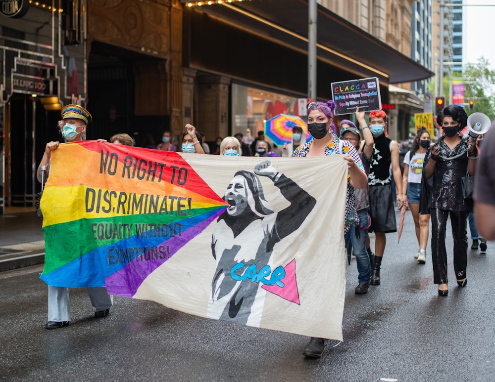 um grupo de pessoas andando por uma rua segurando uma bandeira do arco-íris