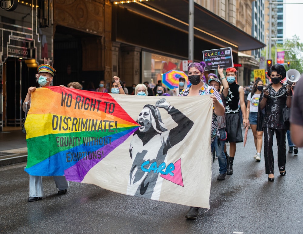 Un grupo de personas caminando por una calle con una bandera del arco iris