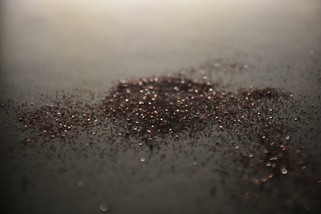 Close-up of finely processed graphite flakes with a factory in the background under soft industrial lighting.