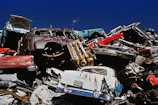 Stack of old scrap cars ready for removal under a bright blue sky.