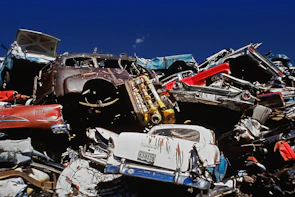 Stack of old scrap cars ready for removal under a bright blue sky.