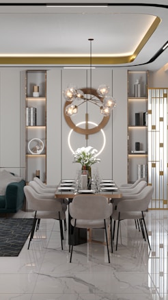 A modern dining room with a long table set for six, featuring elegant minimalist chairs and a striking geometric chandelier with spherical bulbs. The room has built-in shelving units with decorative items and books, and a comfortable green sofa with a geometric rug on the side. The floor is glossy marble with a subtle pattern, adding a touch of luxury.