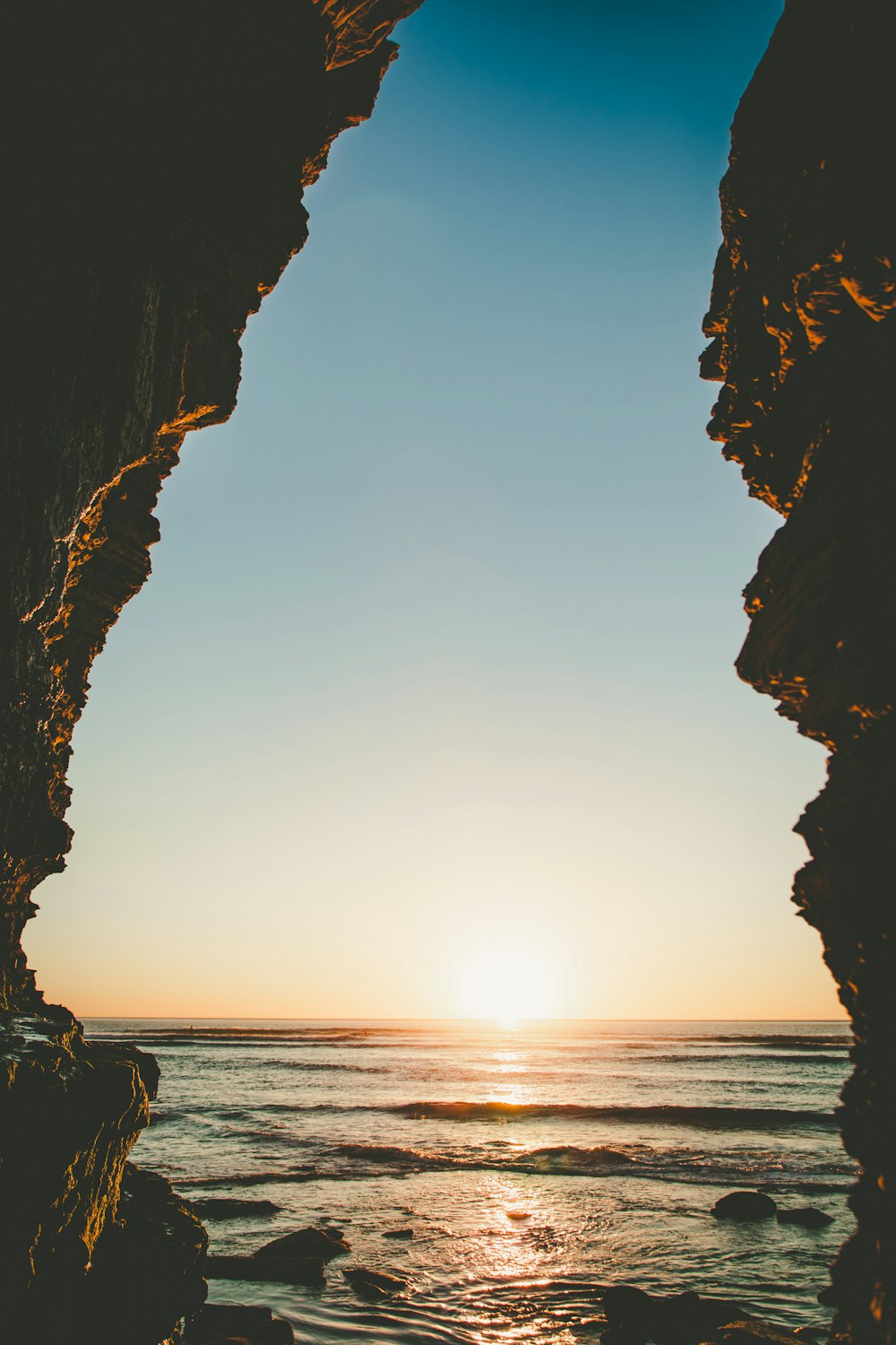 the sun is setting over the ocean from a cave