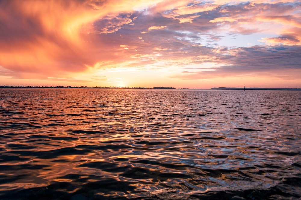un coucher de soleil sur un plan d’eau avec un bateau au loin