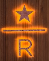A wooden background features a prominent illuminated star above a horizontal line and the letter R. The star and letter are made from a textured metallic material, with an orange glow emanating from behind.