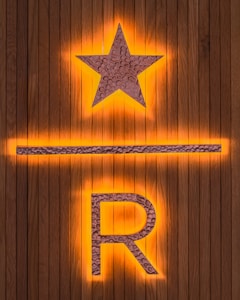A wooden background features a prominent illuminated star above a horizontal line and the letter R. The star and letter are made from a textured metallic material, with an orange glow emanating from behind.
