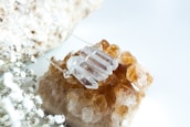 A necklace with several clear, faceted crystal pendants is placed on top of a cluster of amber-hued crystals. In the foreground, delicate white baby's breath flowers are visible, adding a soft, natural touch to the composition.