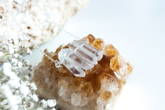 A necklace with several clear, faceted crystal pendants is placed on top of a cluster of amber-hued crystals. In the foreground, delicate white baby's breath flowers are visible, adding a soft, natural touch to the composition.