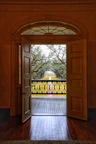 Rustic wooden door opening to a balcony overlooking lush pine trees at sunset.