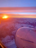 A panoramic view from a private jet window showing a golden sunset over mountains.