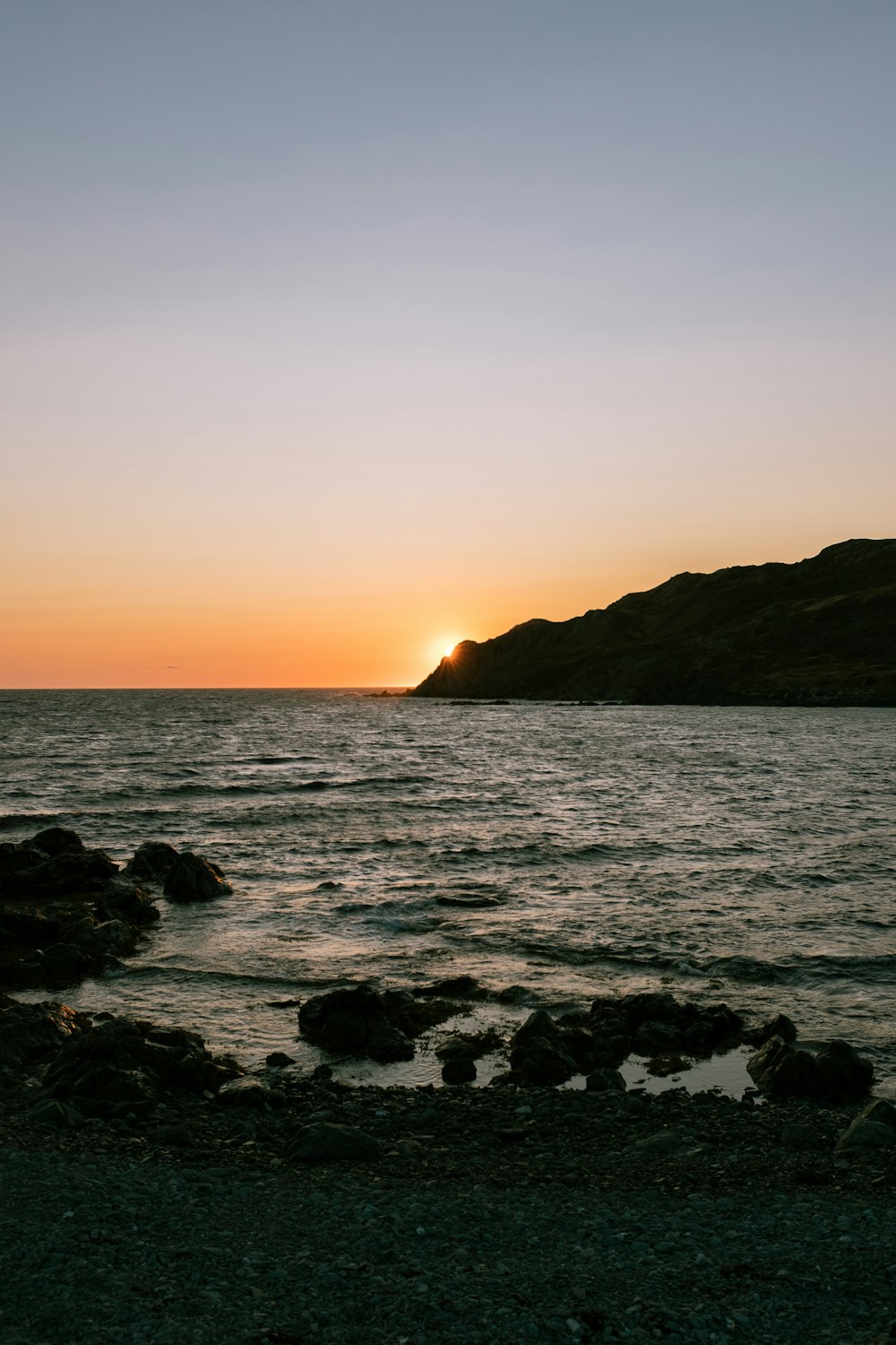 the sun is setting over the ocean with rocks in the foreground