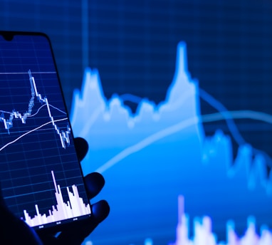 a person holding a cell phone in front of a stock chart