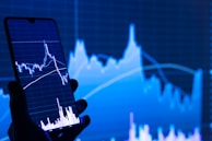 a person holding a cell phone in front of a stock chart