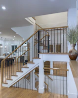 Before-and-after photo showing a sleek wooden staircase with modern metal railings in a bright Roslyn Heights living room