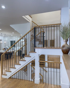 Before-and-after photo showing a sleek wooden staircase with modern metal railings in a bright Roslyn Heights living room