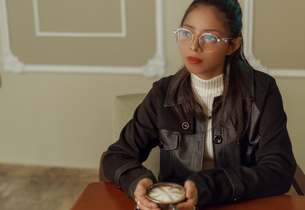 a girl wearing glasses sitting at a table with a clock