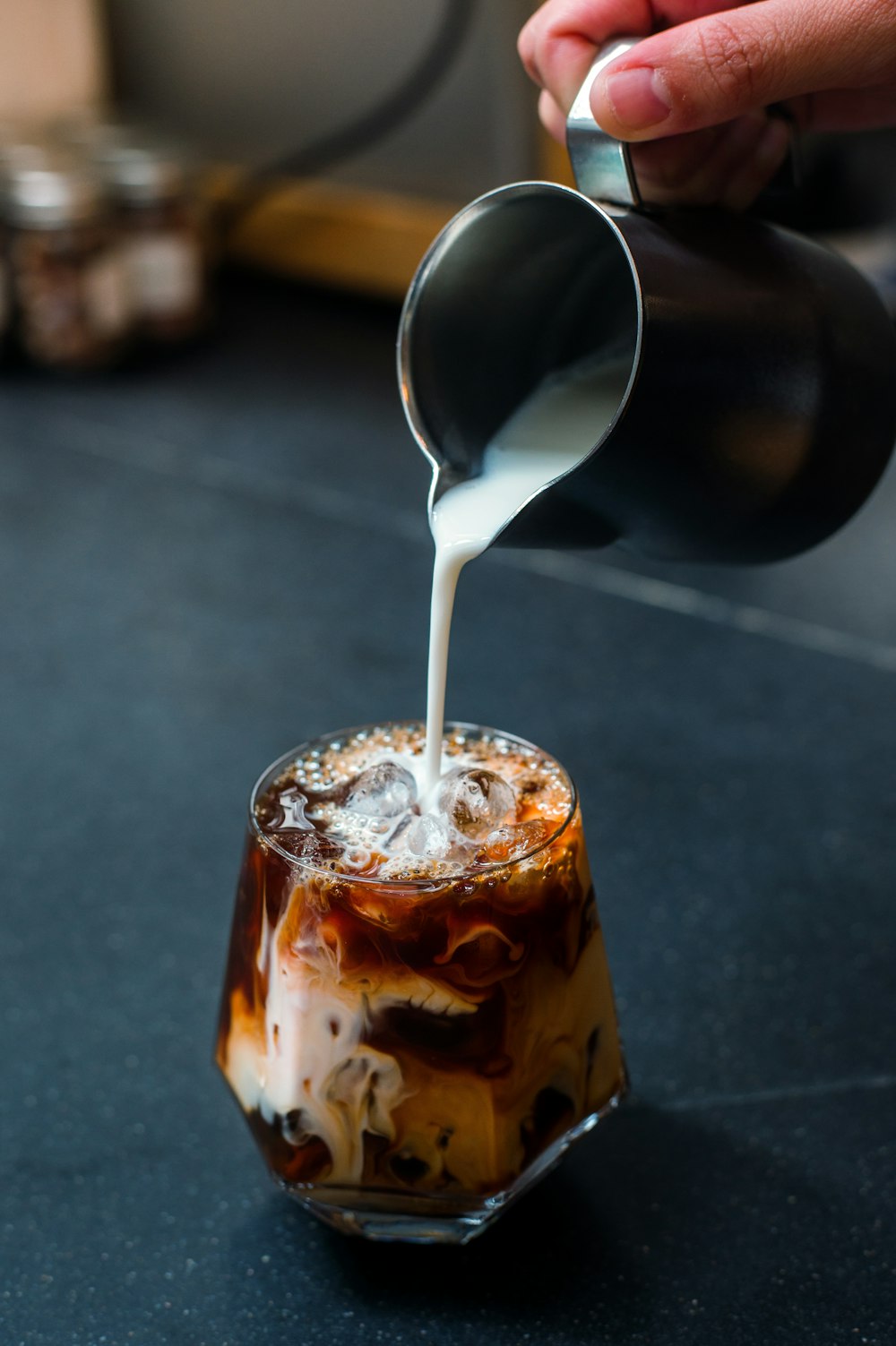 a person pouring milk on top of a drink