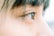 A close-up side view of a person's eye with focus on the eyelashes and eyebrow. The background is blurred, emphasizing the details of the eye and surrounding skin.