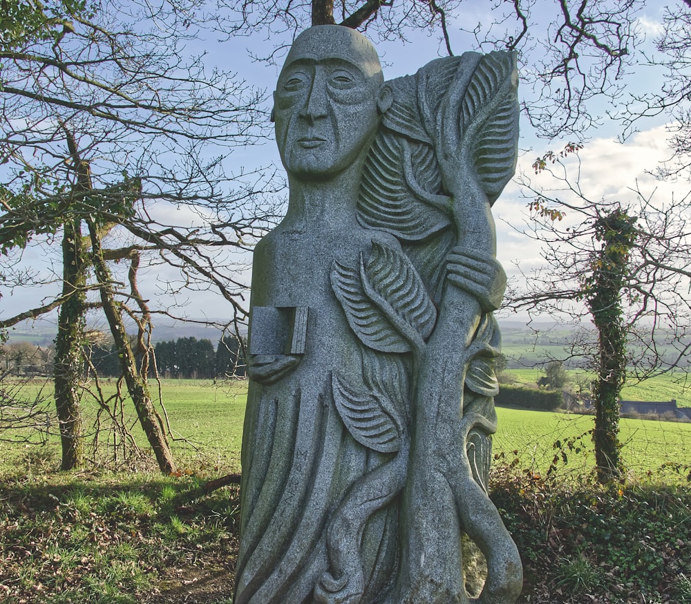 a statue of a woman holding a plant in a field