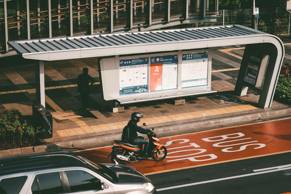 a man riding a motorcycle down a street next to a bus stop