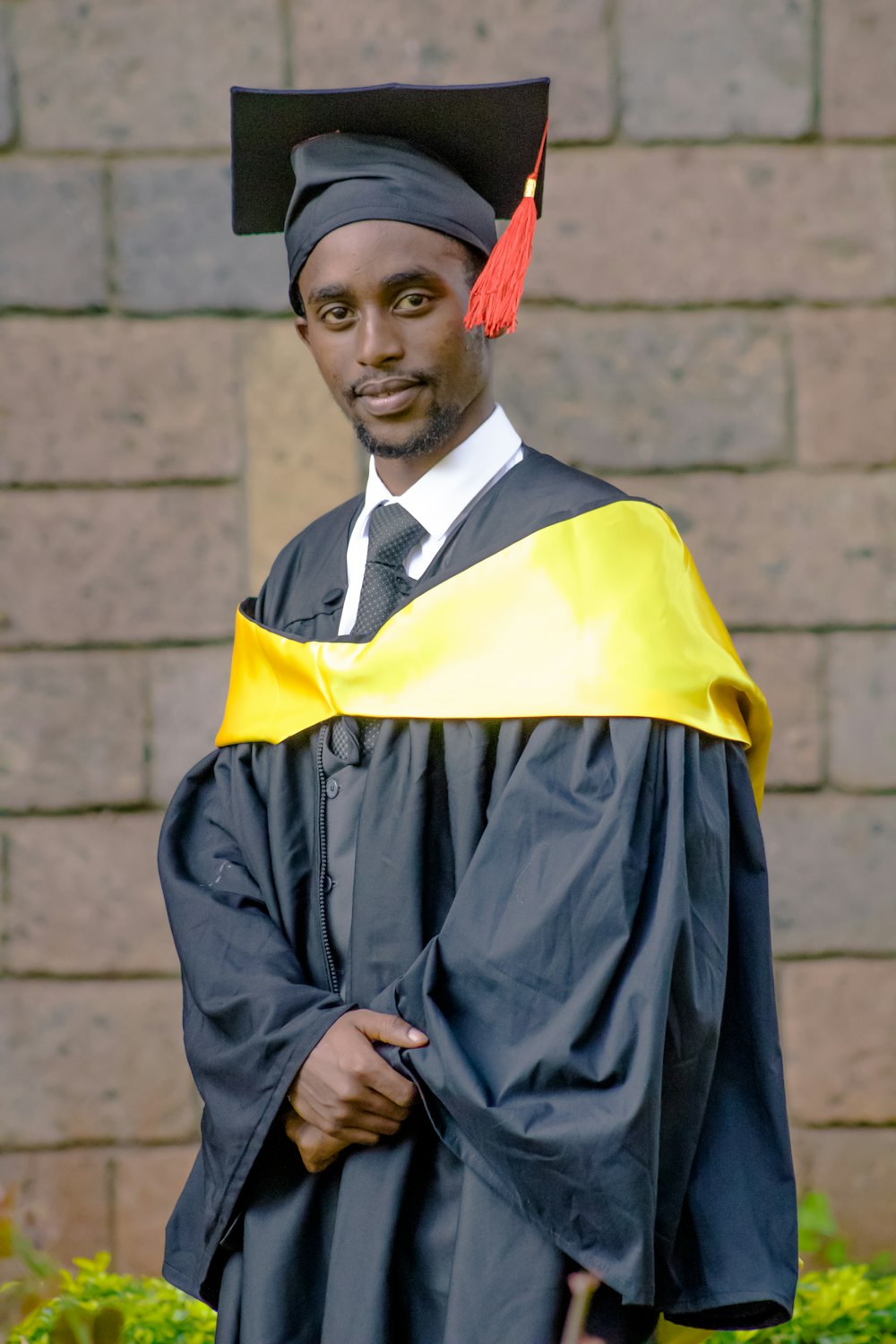 a man in a cap and gown standing in front of a brick wall