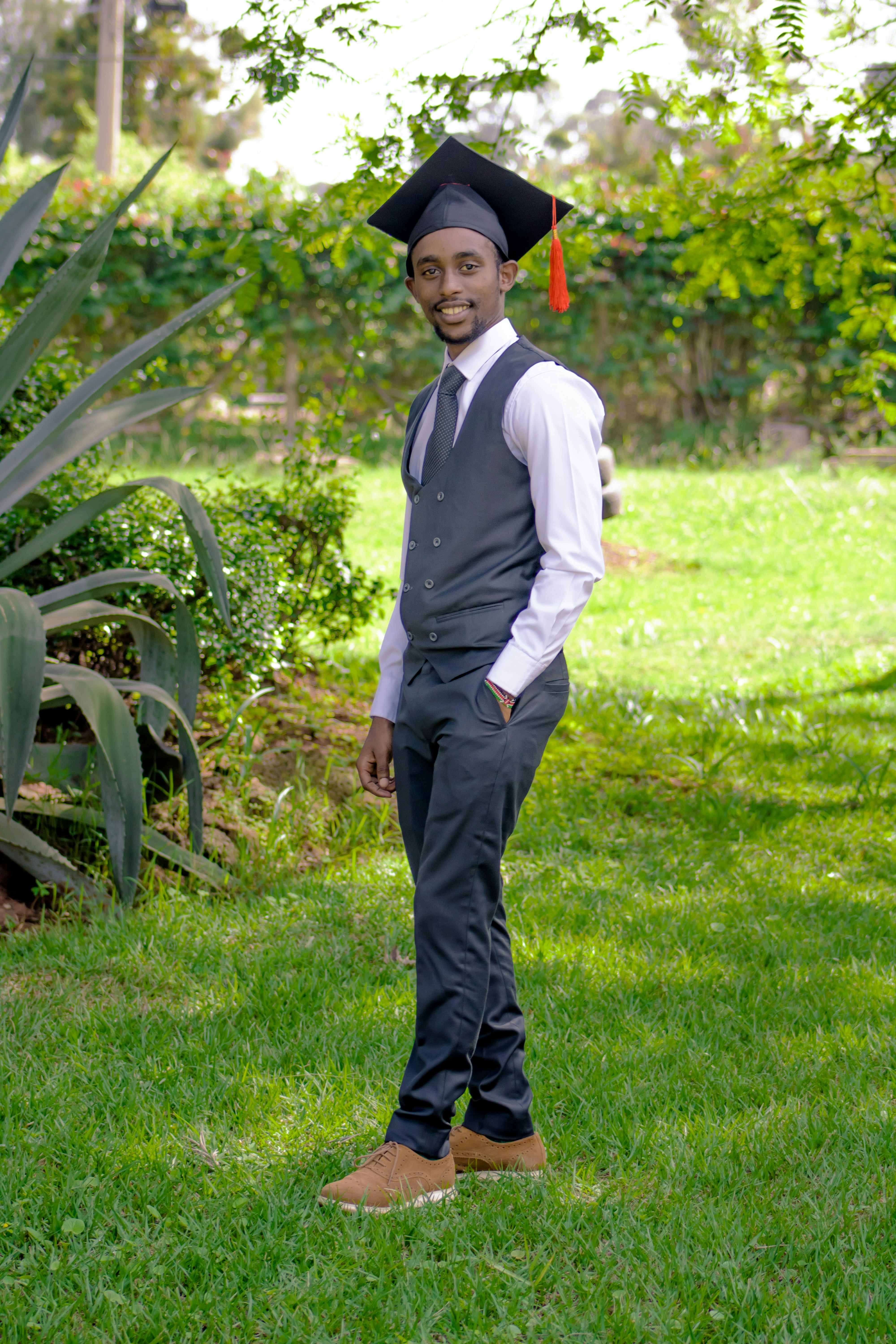 a man in a graduation cap and gown standing in the grass