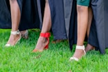 A close-up view of people wearing stylish shoes, featuring various high heels in red, white, and silver against a vibrant green grass background with black fabric draped around.