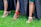 A close-up view of people wearing stylish shoes, featuring various high heels in red, white, and silver against a vibrant green grass background with black fabric draped around.