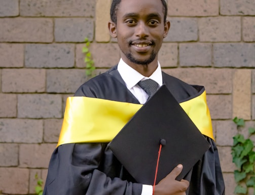 a man in a graduation gown holding his cap and gown