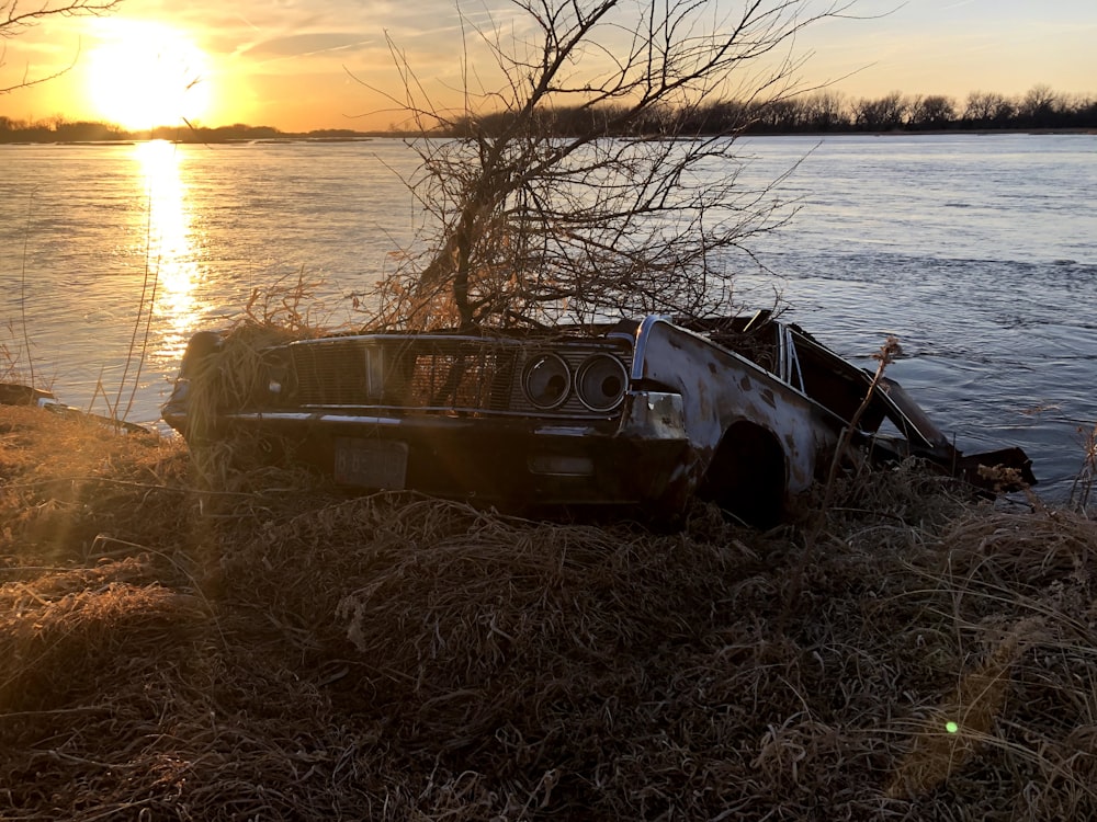 a rusted car sitting on top of a dry grass field next to a body