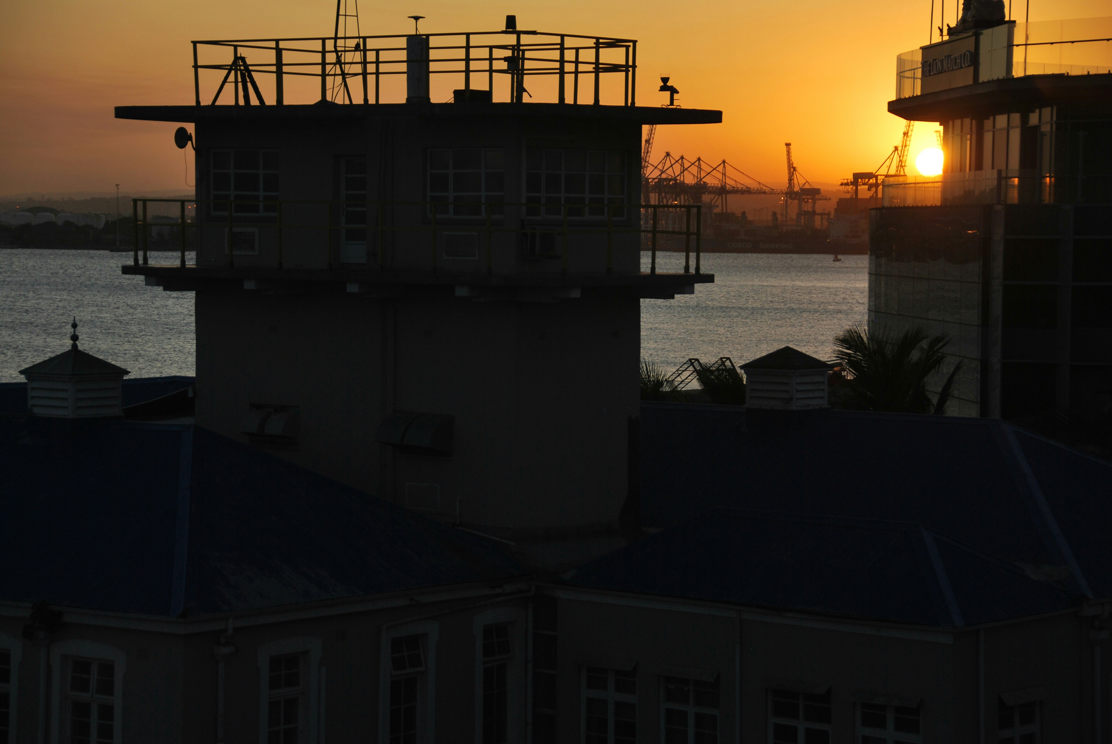 the sun is setting over the water behind a building