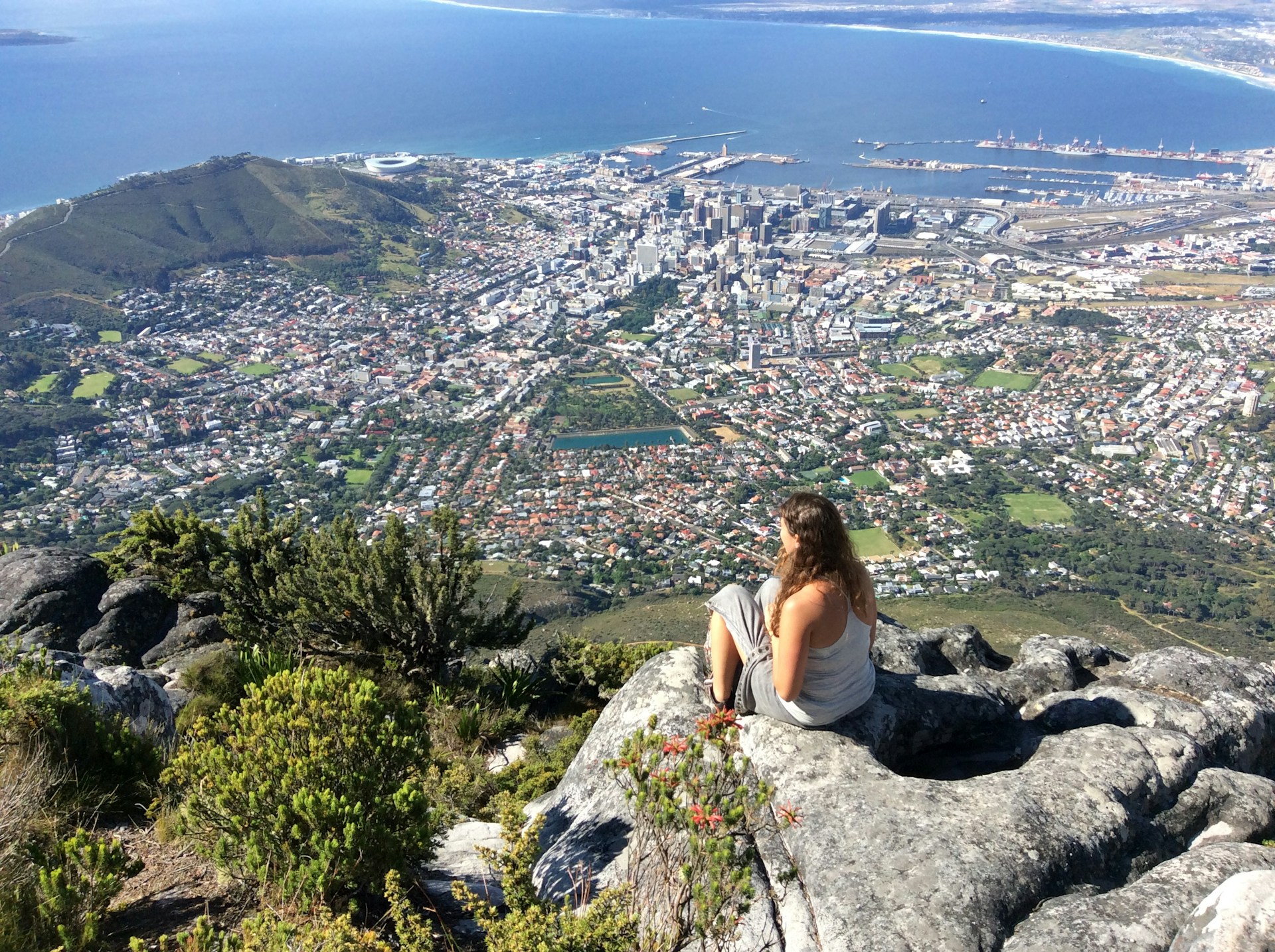 a woman sitting on top of a mountain overlooking a city