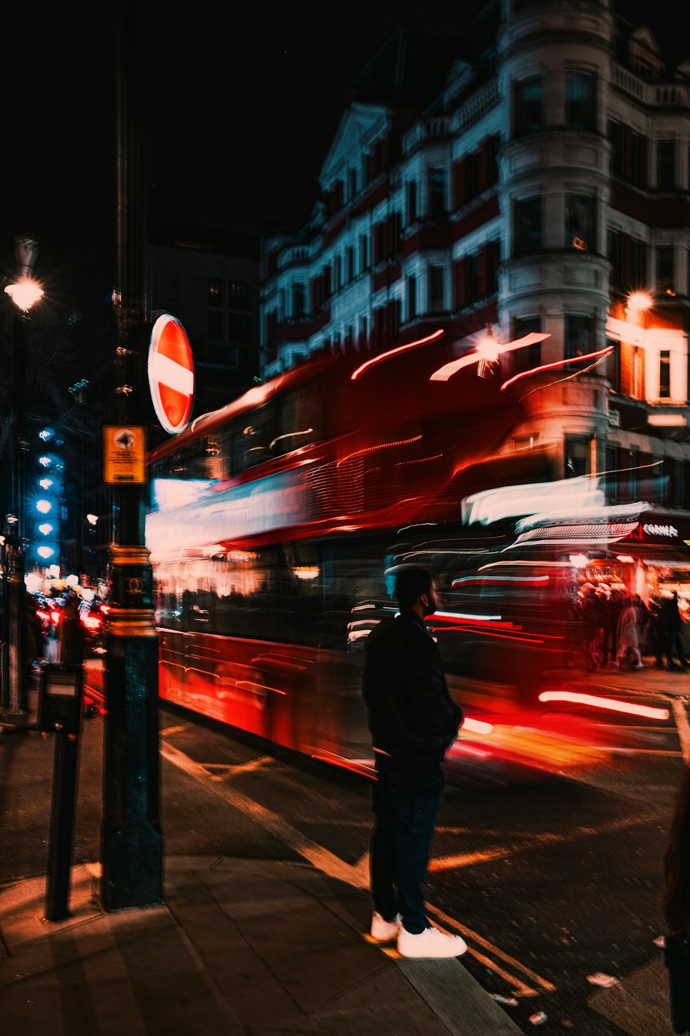 a man standing on the side of a street next to a red double decker bus