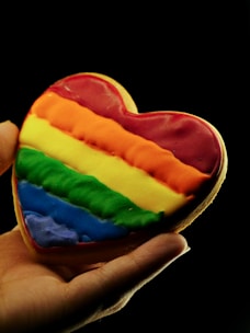 a rainbow heart shaped cookie being held by a hand