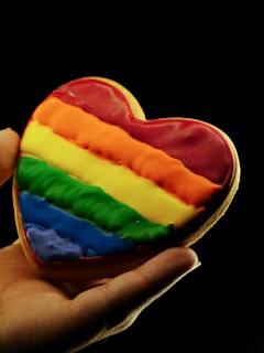 a rainbow heart shaped cookie being held by a hand
