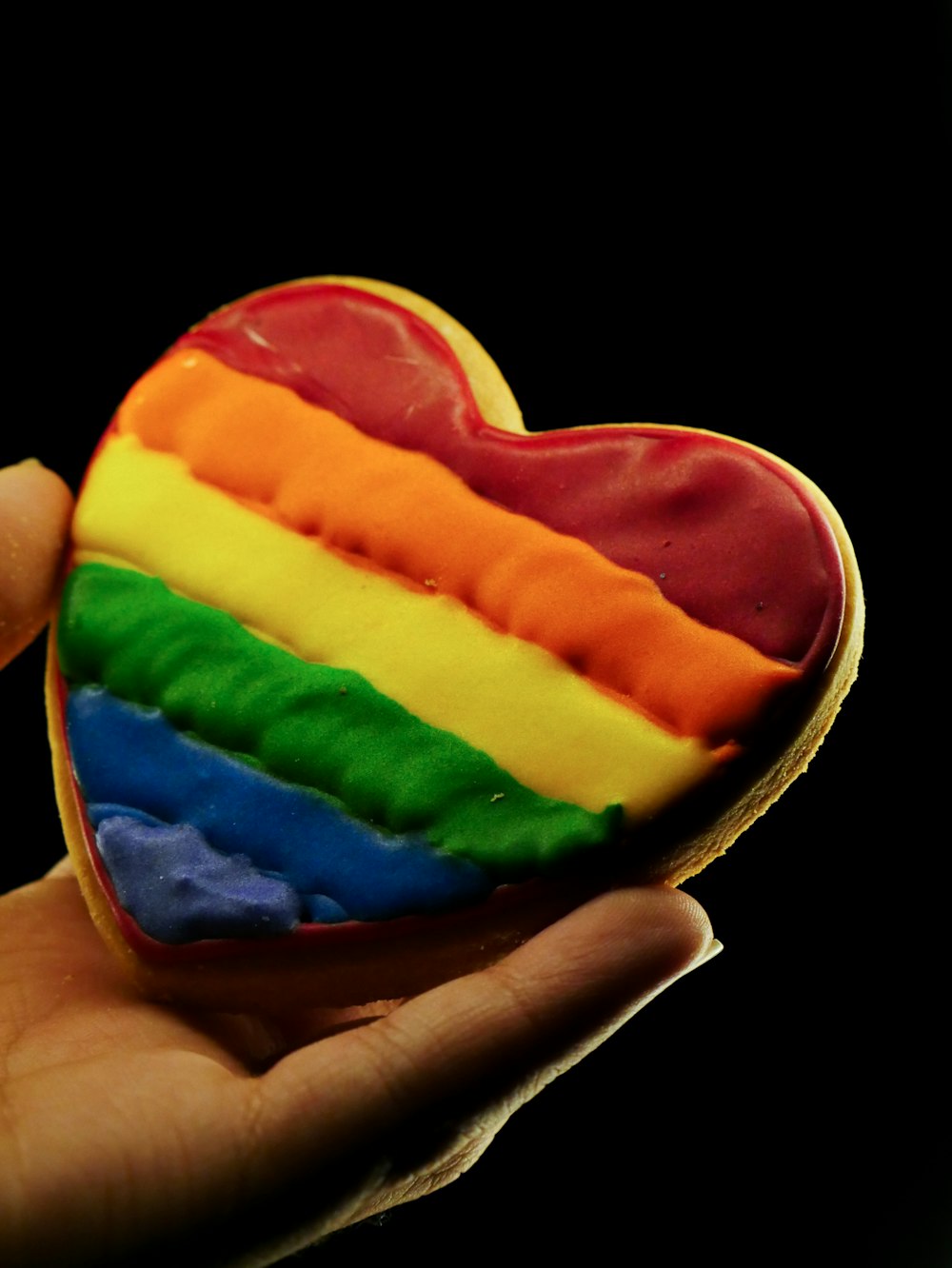 a rainbow heart shaped cookie being held by a hand