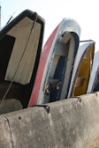 Several boats are placed vertically against a concrete barrier, with visible wear and paint peeling from their surfaces. The boats are lined up closely, showcasing various colors and the ropes hanging loosely.