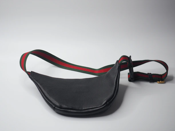 Close-up of a sleek black mini waist pack worn by a person walking through a city park.
