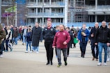 A bustling crowd of people walking outside, with some wearing sports jerseys. The background features an urban environment with construction scaffoldings. The atmosphere is lively and casual, suggesting perhaps an event or gathering.