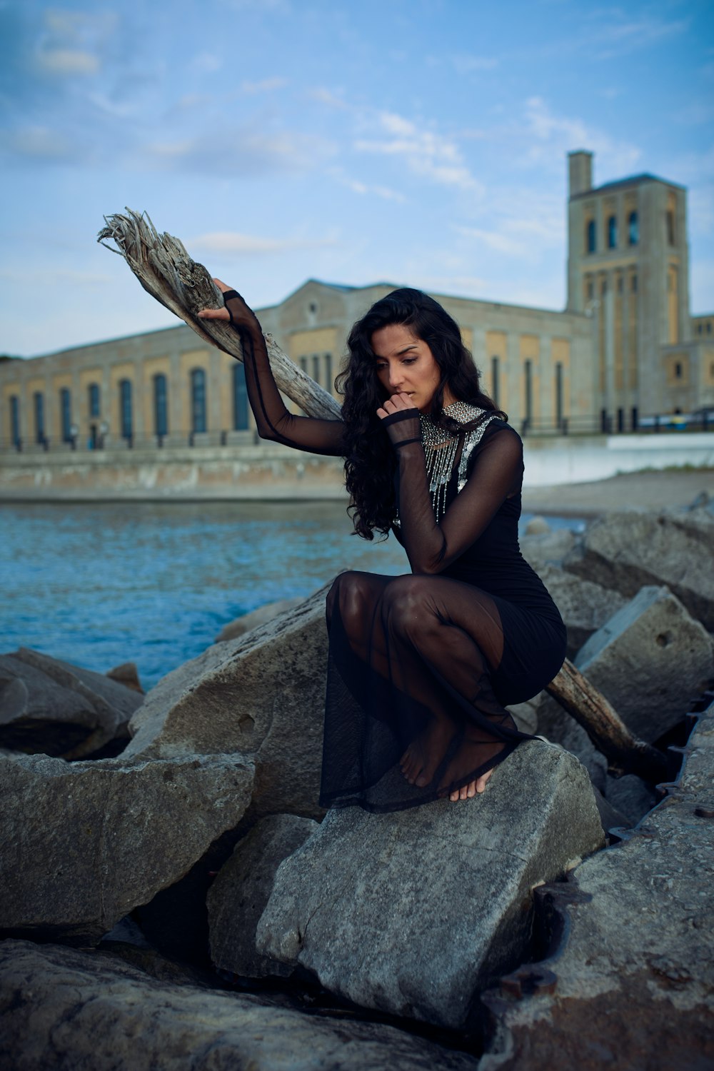 a woman sitting on a rock next to a body of water