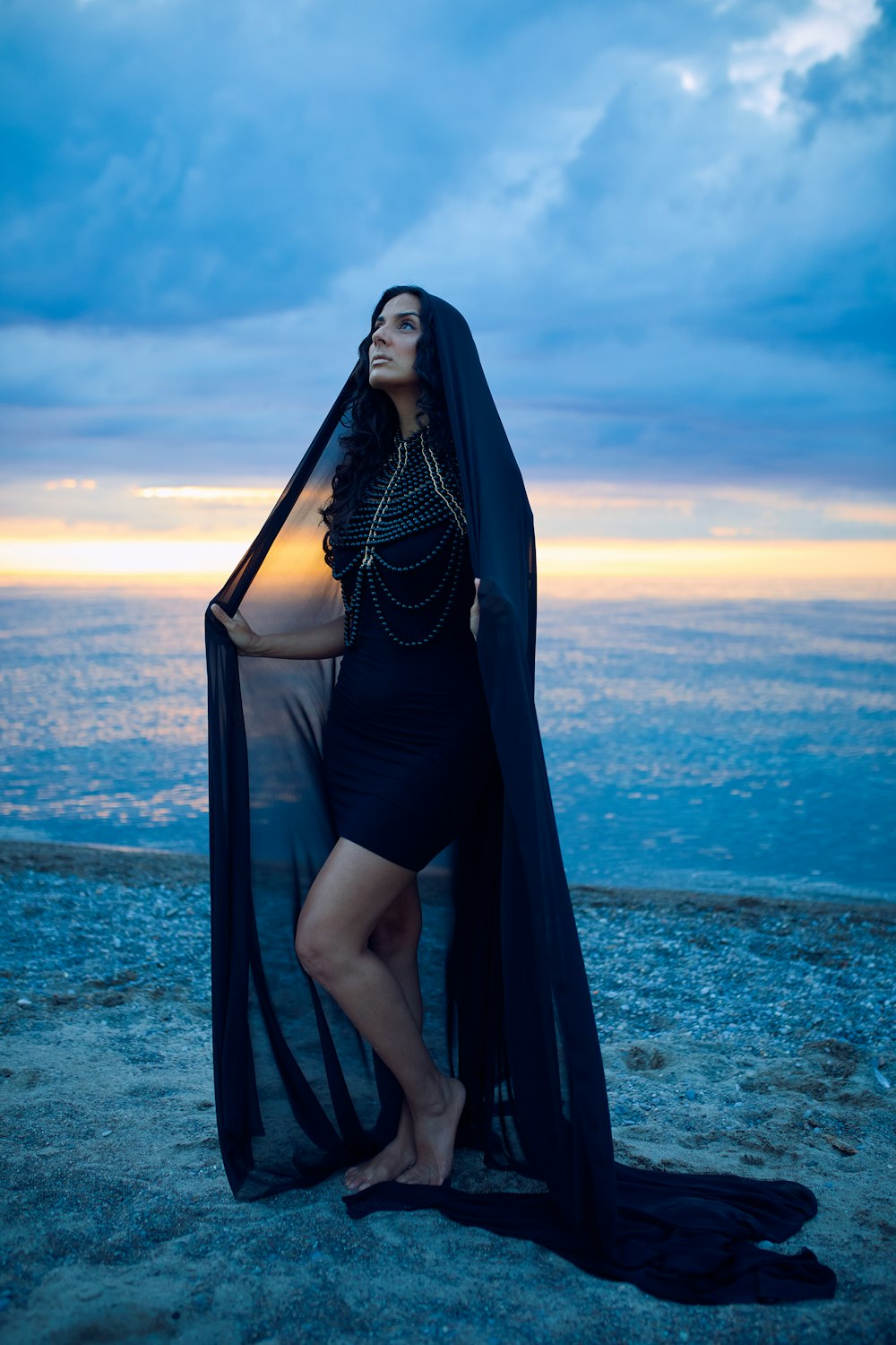 uma mulher em um vestido preto em pé em uma praia