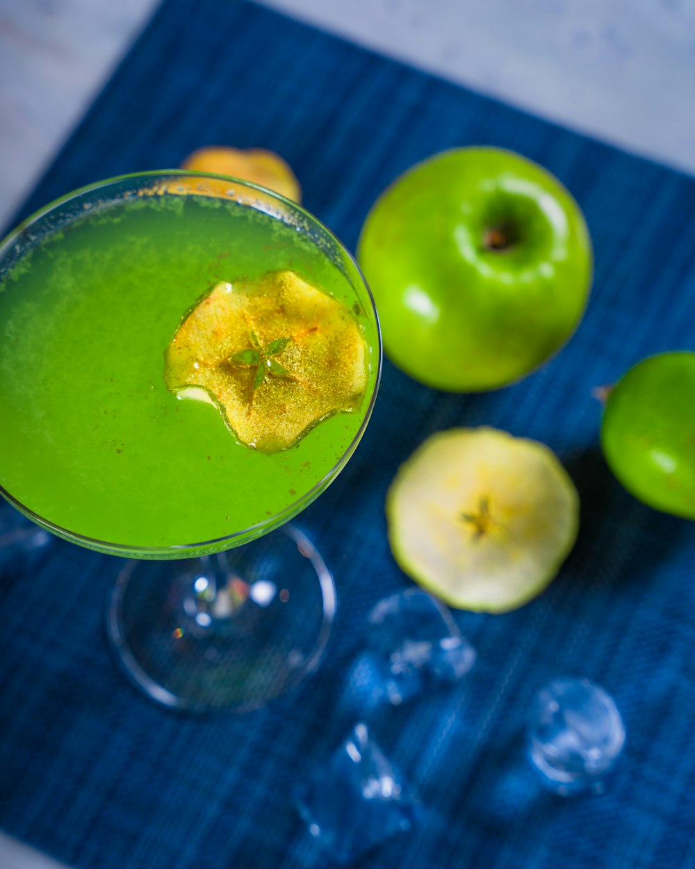 a green drink in a glass next to two green apples