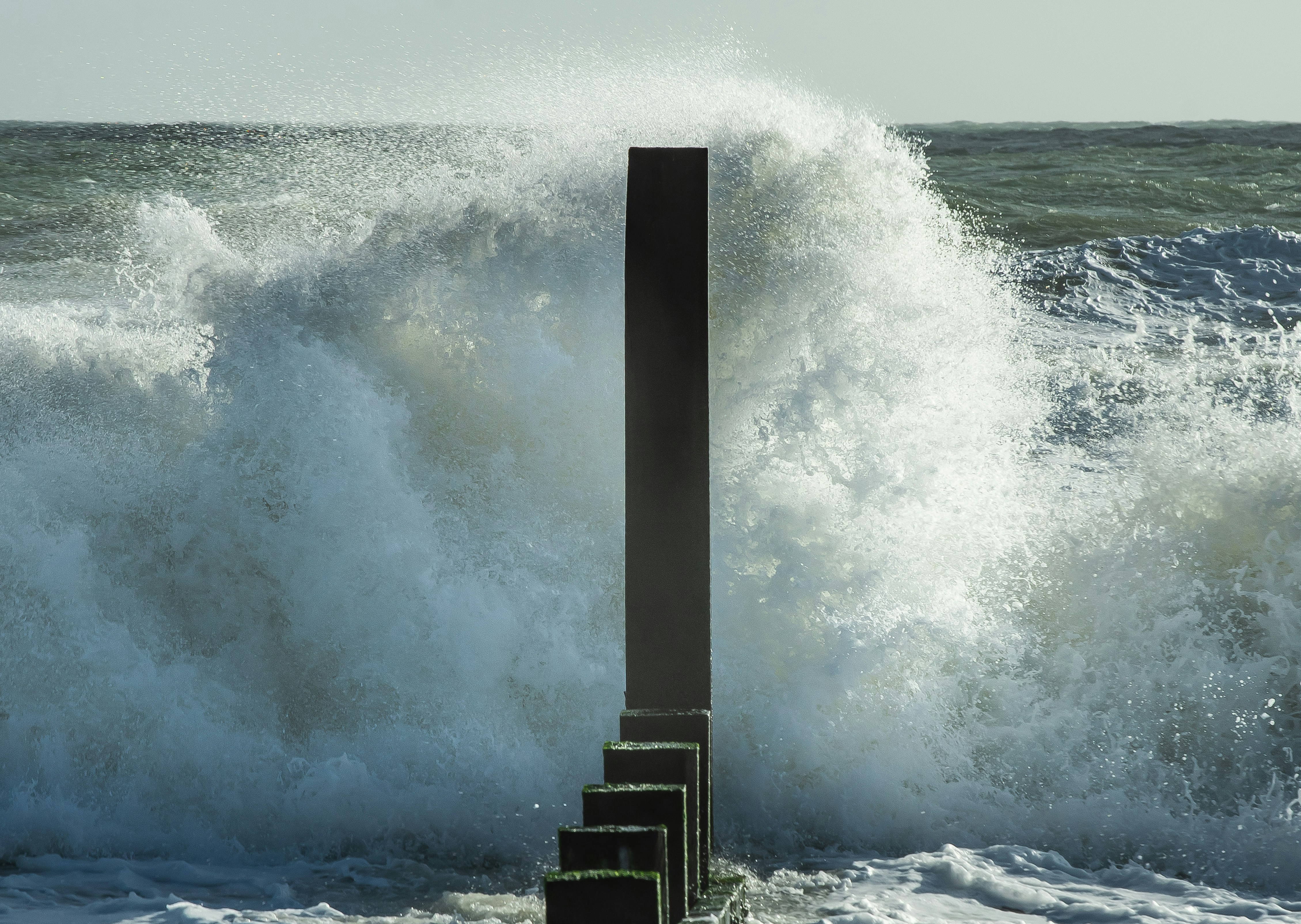 a large wave crashing over a metal pole