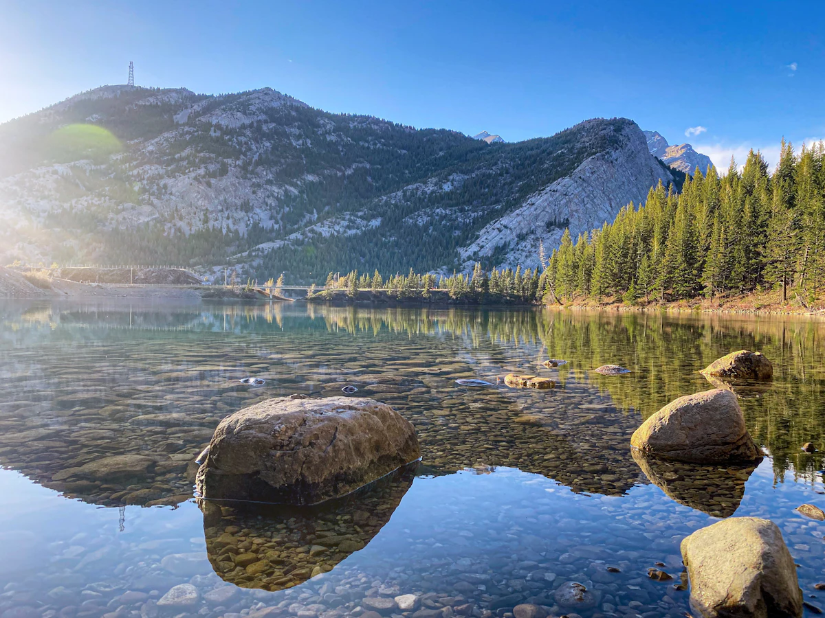 Boulders in the clear water of Emerald Lake in Crowsnest Pass, below a forested mountain