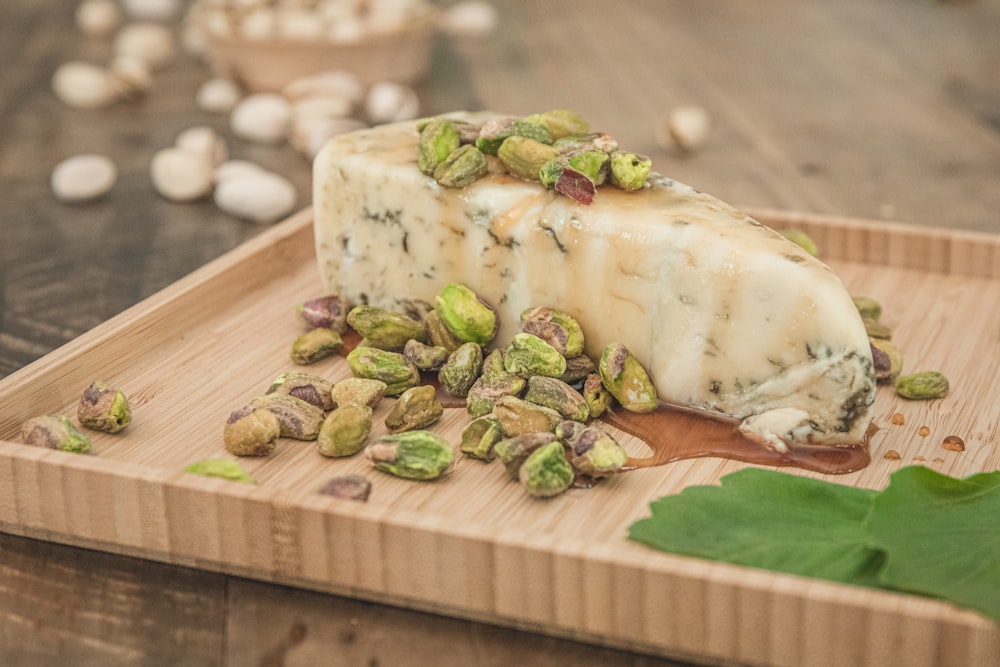 a piece of cheese with pistachios on a cutting board