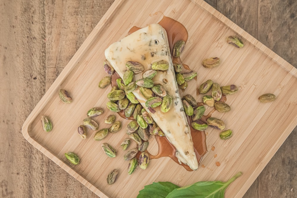 a piece of cheese with pistachios on a cutting board