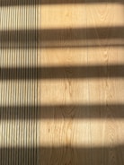 Wooden flooring with alternating vertical slats on the left side. Shadows cast across the surface, creating a pattern of light and dark bands.