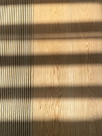 Wooden flooring with alternating vertical slats on the left side. Shadows cast across the surface, creating a pattern of light and dark bands.