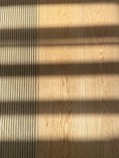 Wooden flooring with alternating vertical slats on the left side. Shadows cast across the surface, creating a pattern of light and dark bands.