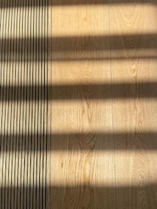 Wooden flooring with alternating vertical slats on the left side. Shadows cast across the surface, creating a pattern of light and dark bands.